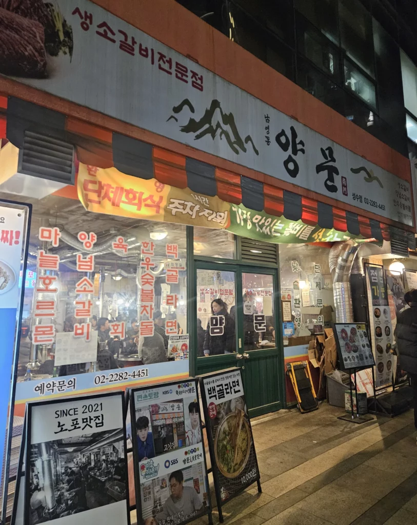 Exterior of a busy Korean BBQ restaurant at night, featuring signage and diners inside, known for grilled beef Korean BBQ and charcoal-grilled ribs.