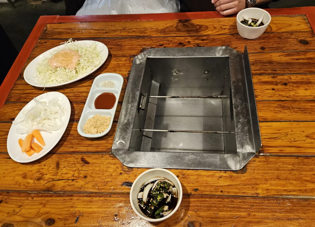 Table setup at a Yongsan smoked K-BBQ restaurant with built-in charcoal grill, fresh vegetables, dipping sauces, and side dishes prepared for an authentic Korean barbecue experience.