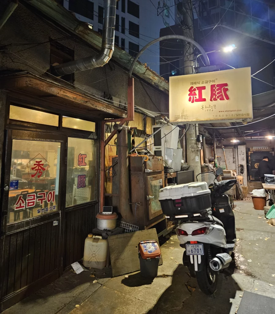 Exterior of a traditional smoked K-BBQ restaurant in Yongsan at night, featuring vintage Korean signage, narrow alley surroundings, and the authentic local atmosphere of Seoul’s hidden dining spots.