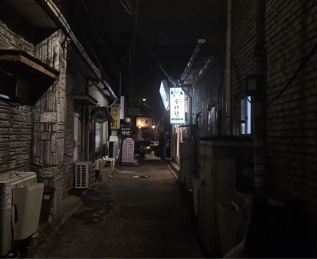 Narrow back alley in Yongsan at night lined with old restaurants and signboards, capturing the hidden local vibe where smoked K-BBQ spots are tucked away in Seoul’s traditional dining streets.