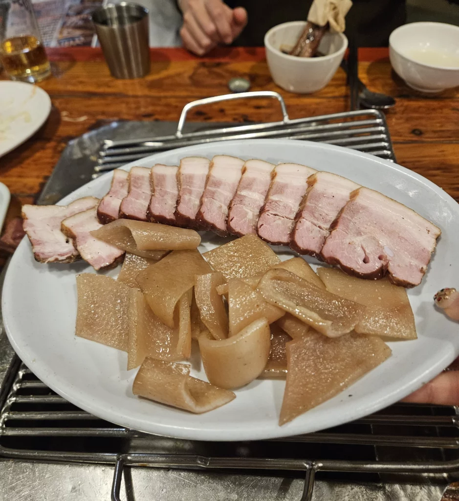 Sliced smoked pork served with tender radish pieces on a grill at a local restaurant in Yongsan, showcasing authentic smoked K-BBQ with rich flavor and traditional Korean presentation.