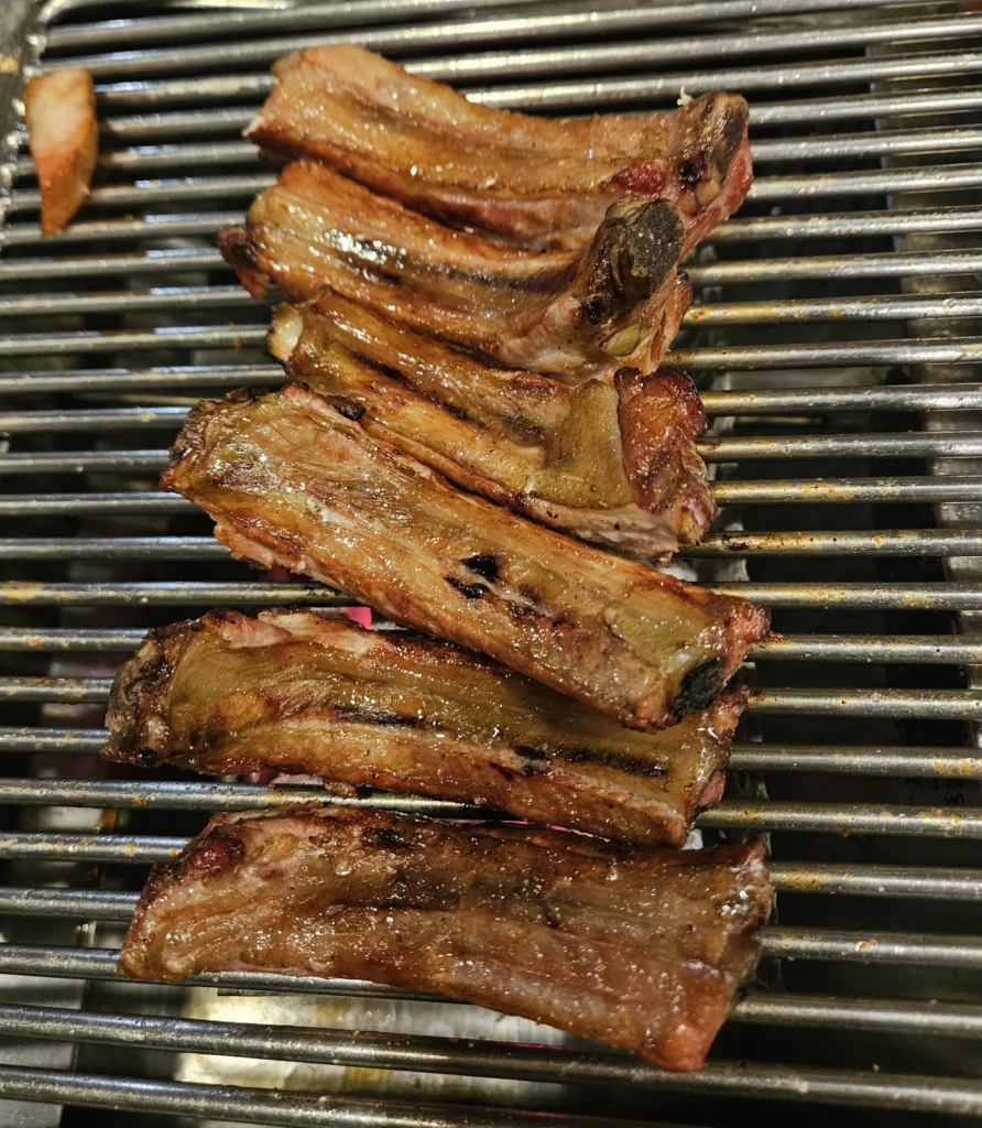 Thick-cut smoked pork ribs grilling over charcoal at a Yongsan restaurant, showcasing authentic smoked K-BBQ with crispy exterior, juicy meat, and deep wood-smoked flavor.
