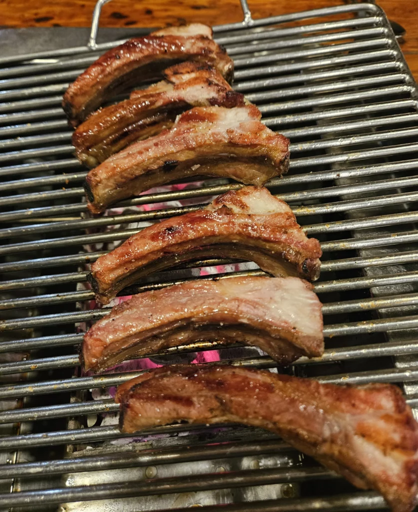 Thick slices of smoked pork ribs grilling over charcoal at a Yongsan restaurant, showcasing glossy fat layers and deep smoky flavor typical of authentic smoked K-BBQ.