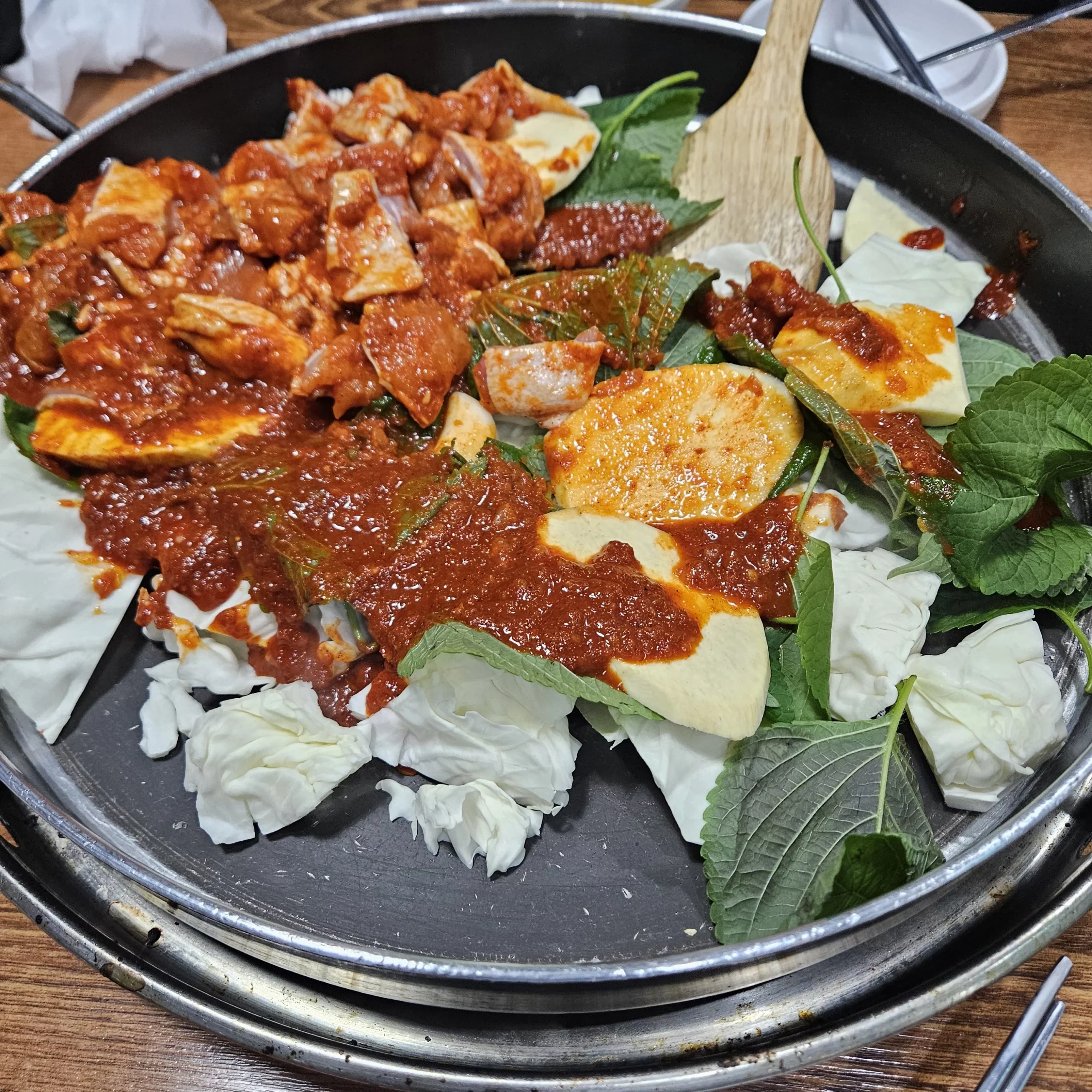 Uncooked ingredients for stir-fried chicken Okeunnae Dakgalbi arranged on a large pan with marinated chicken, cabbage, perilla leaves, and spicy red sauce.