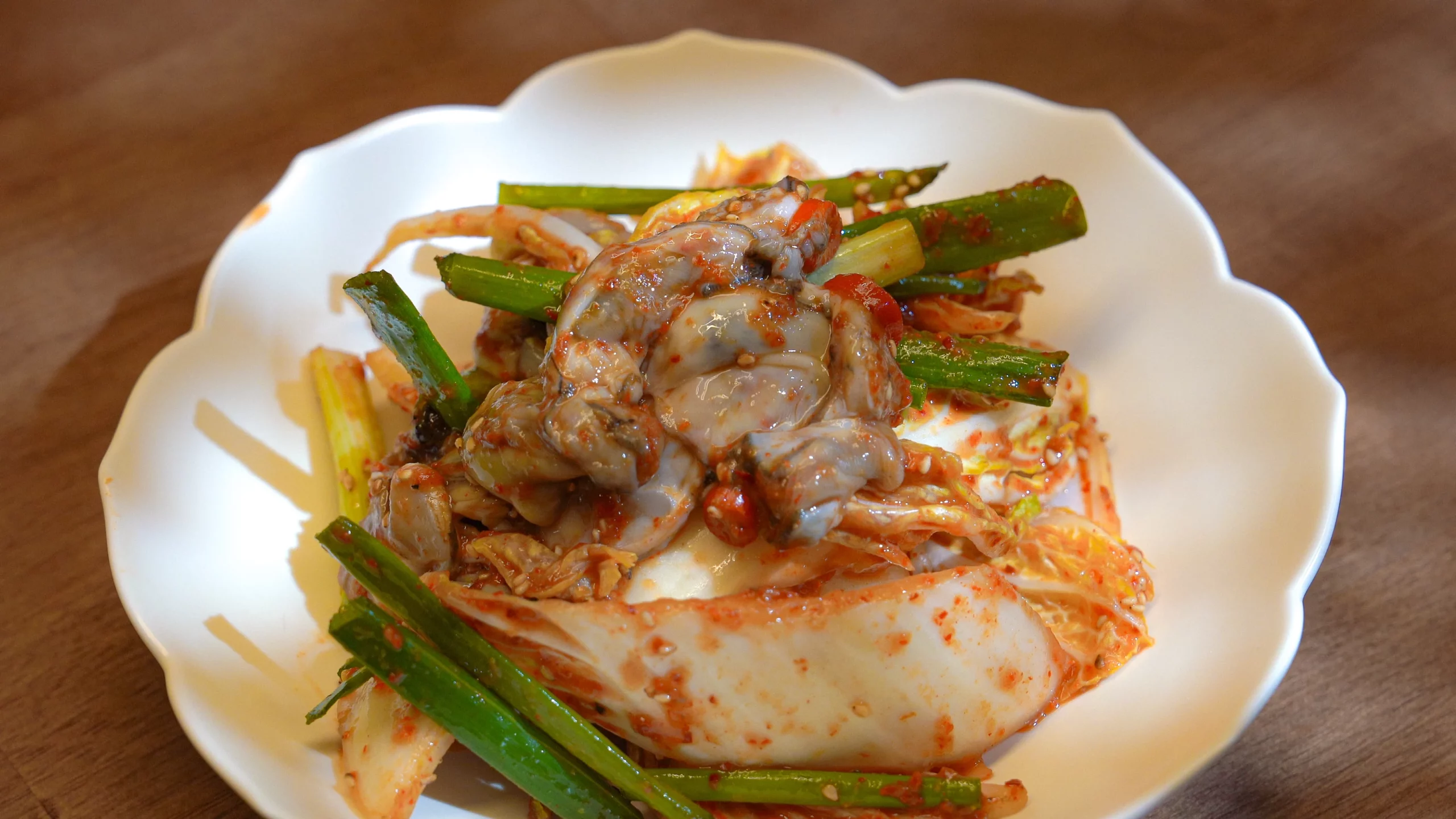 Finished Korean oyster geotjeori with fresh oysters, scallions, and red pepper seasoning served on a white plate.