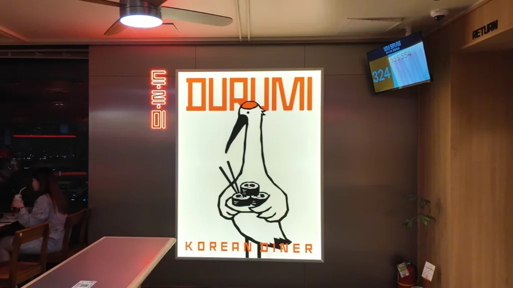 Durumi Bunsik logo sign featuring a red-crowned crane holding gimbap with chopsticks inside the N Seoul Tower restaurant.