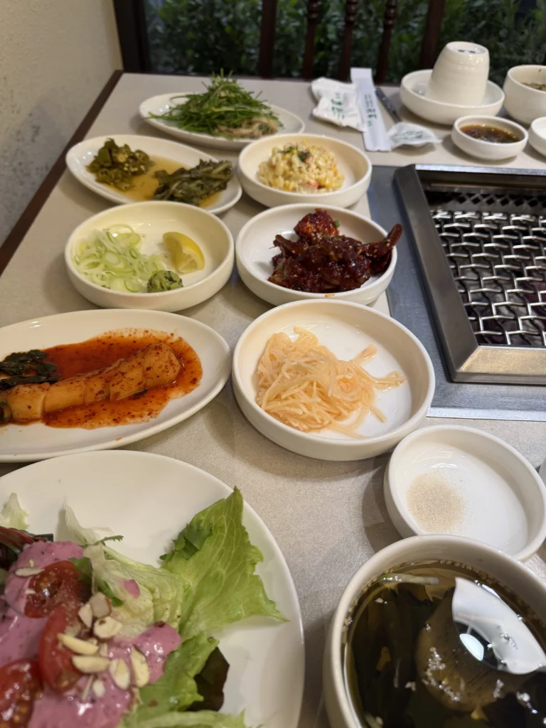 Traditional Korean banchan side dishes spread at Chowon Korean BBQ in Gangnam including kimchi, pickled vegetables, lettuce wraps, and raw marinated beef jumulleok around charcoal grill.