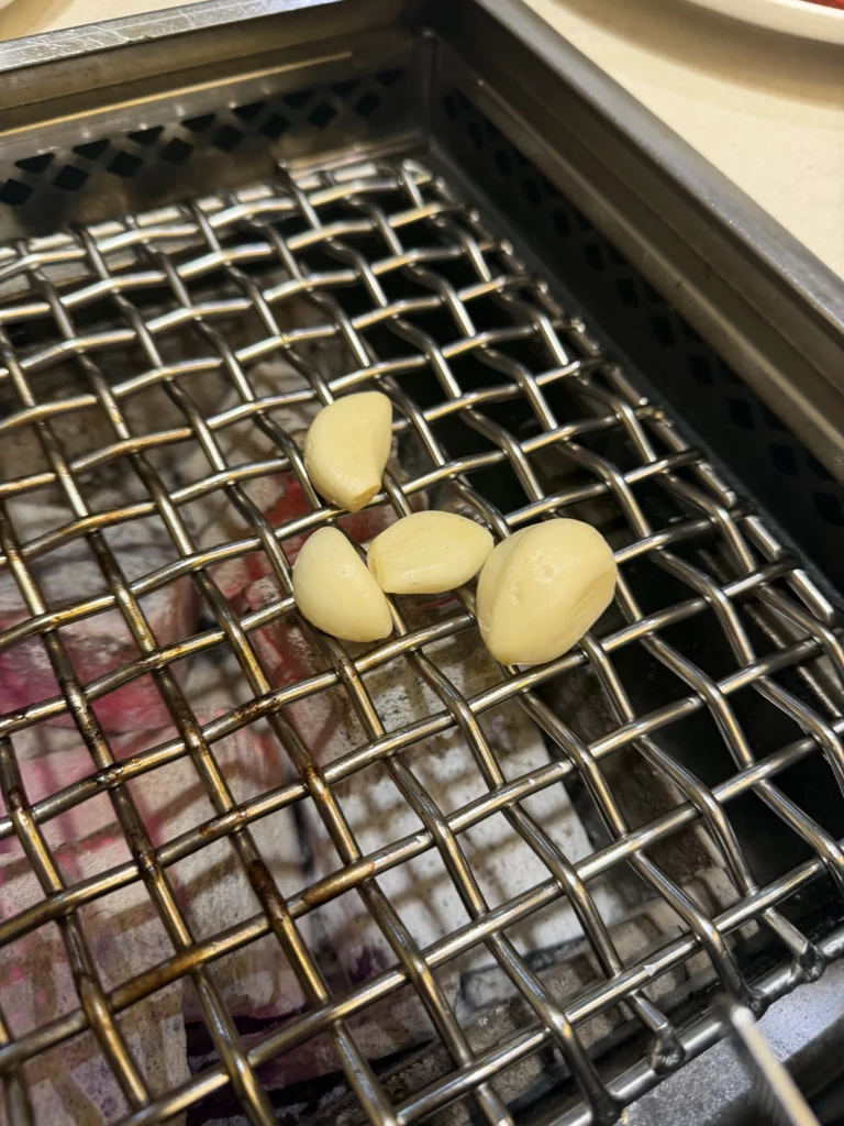 Fresh garlic cloves grilling on charcoal grill alongside marinated beef jumulleok at Chowon Korean BBQ in Gangnam Seoul.