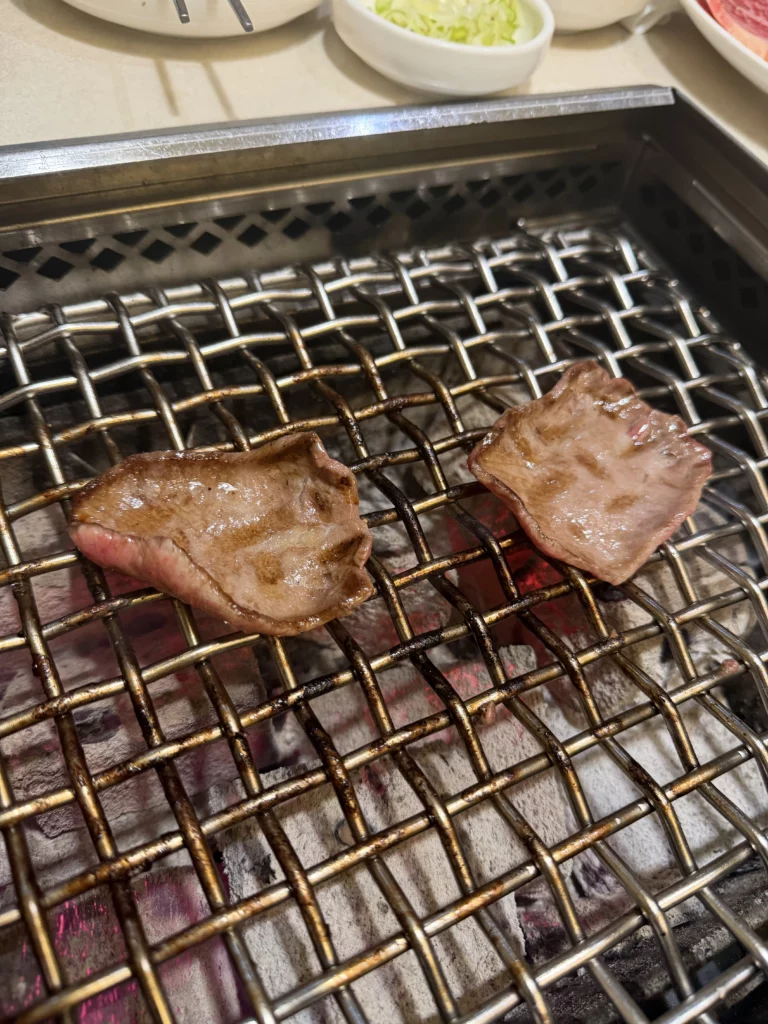 Beef tongue slices grilling with caramelized char marks on charcoal grill at Chowon Korean BBQ in Gangnam Seoul.