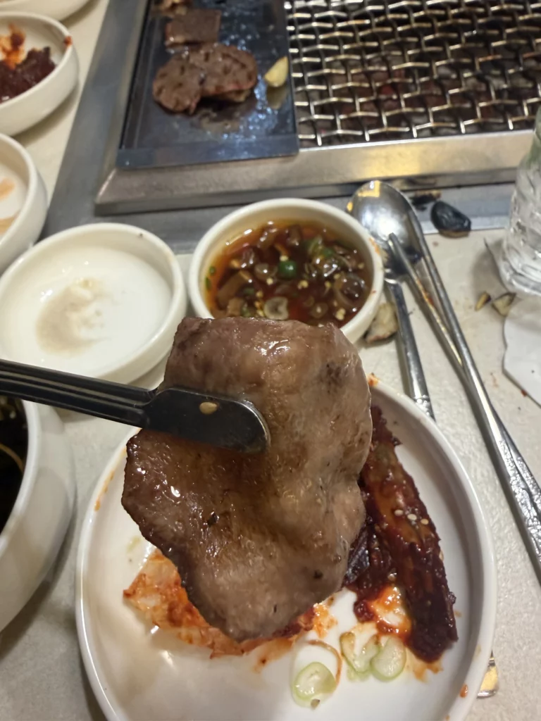 Grilled beef tongue held with chopsticks served with sesame oil salt dipping sauce at Chowon Korean BBQ in Gangnam Seoul.