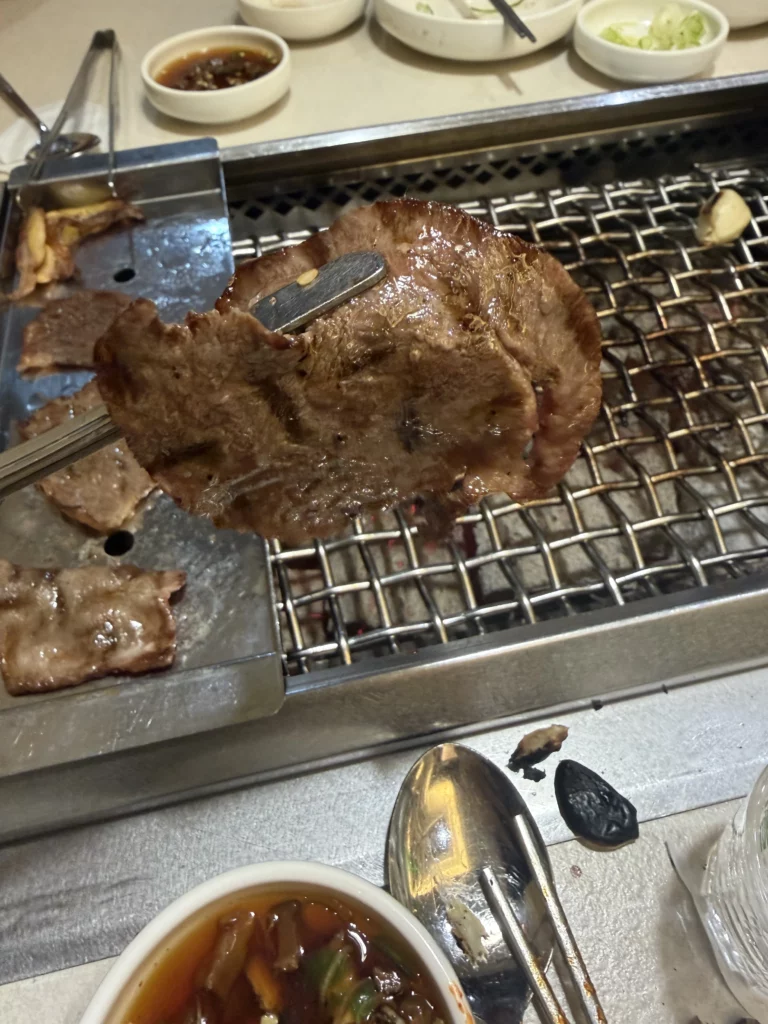 Grilled beef tongue being cut with scissors into bite-sized pieces on charcoal grill at Chowon Korean BBQ in Gangnam Seoul.