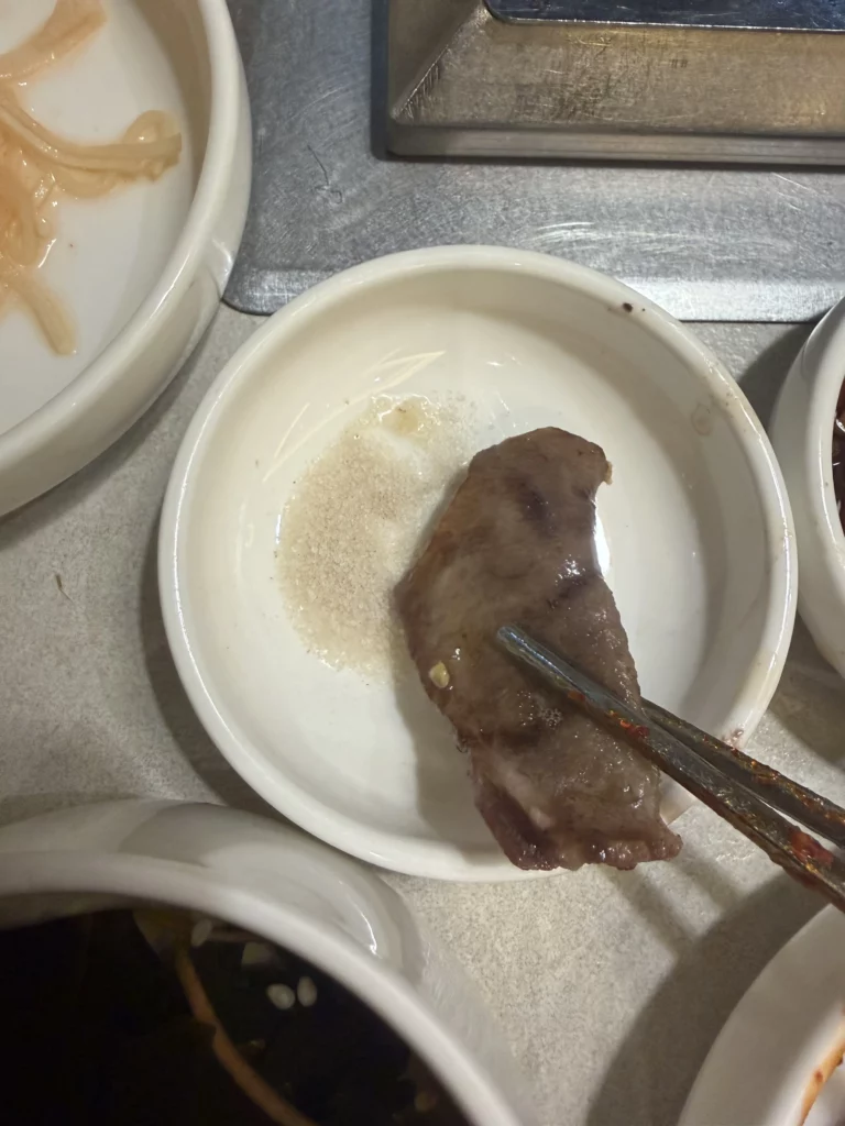 Grilled beef tongue being dipped in sesame oil and salt sauce at Chowon Korean BBQ in Gangnam Seoul.