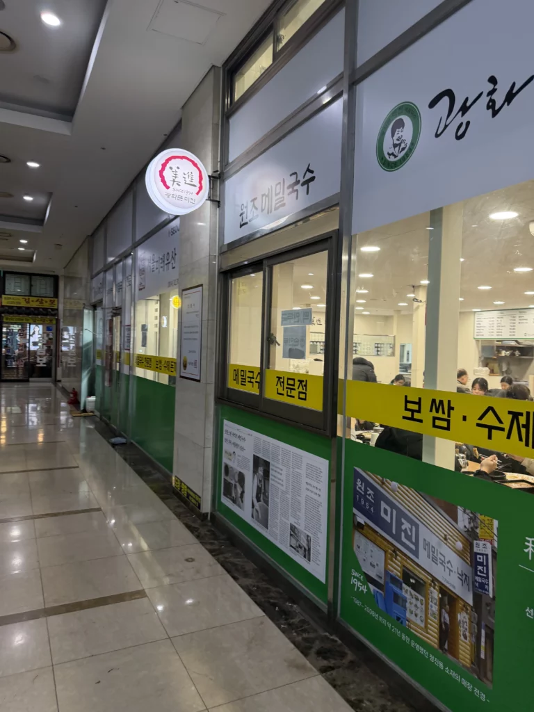 Mijin Korean buckwheat noodle restaurant exterior with green and yellow storefront featuring informational displays and Seoul Future Heritage certification at Lemaire Jongno Town in Pimatgol district.