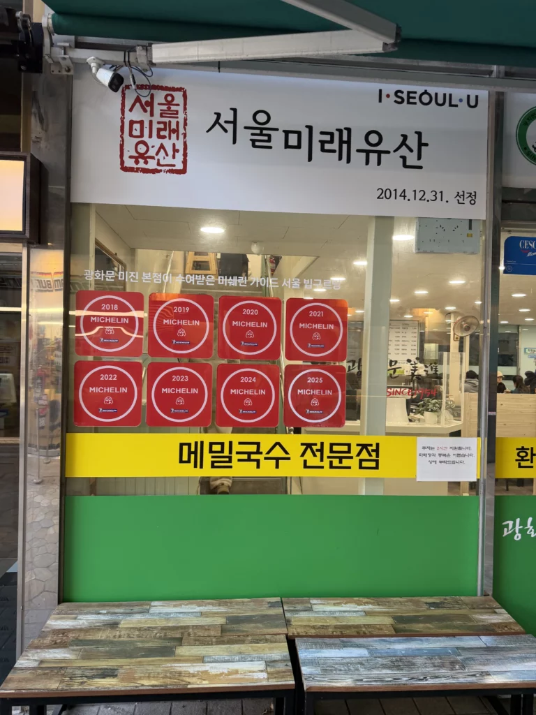Mijin restaurant storefront displaying Seoul Future Heritage designation and eight consecutive Michelin Bib Gourmand recognition plaques from 2018 to 2025, with yellow banner indicating buckwheat noodle specialty in historic Pimatgol, Seoul.