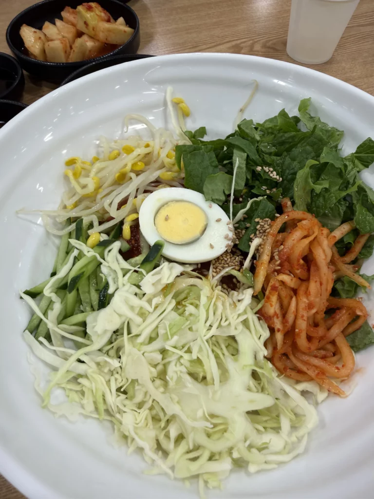 Bibim memil myeon Korean buckwheat noodles with julienned vegetables, soft-boiled egg, bean sprouts, and kimchi before mixing at Mijin Michelin Bib Gourmand restaurant in Seoul.