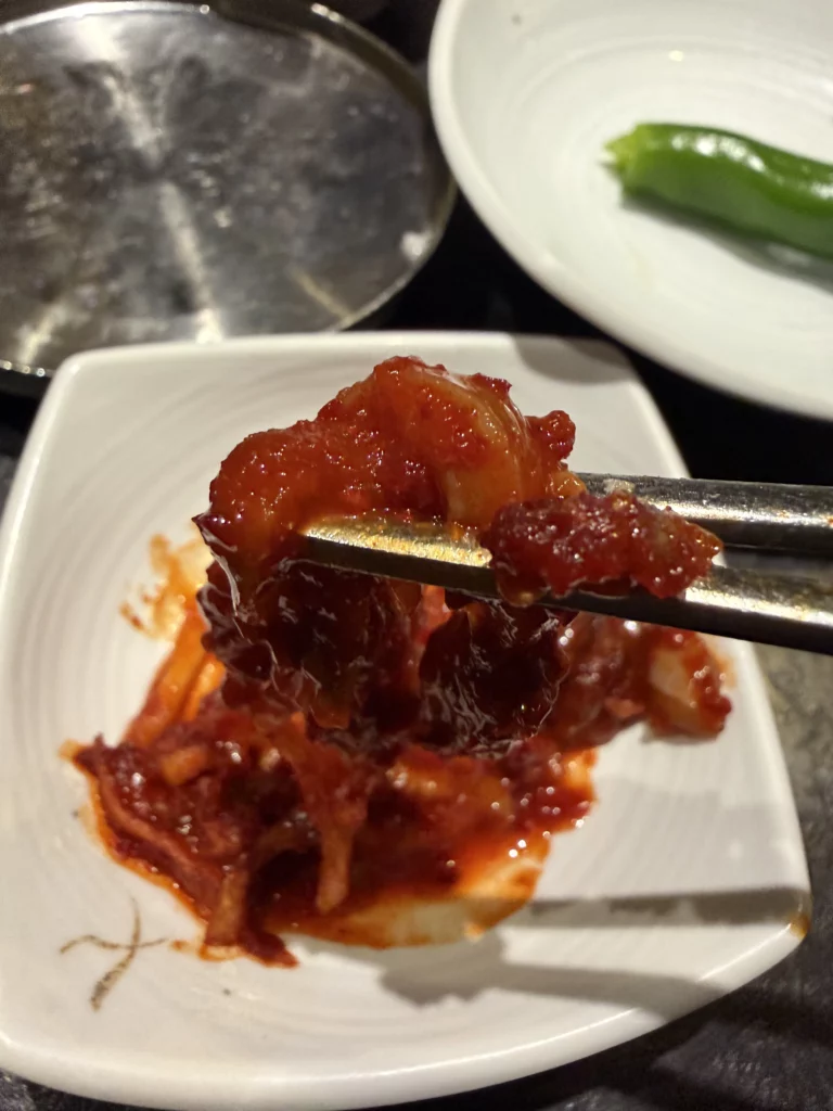 Fermented squid ojingeo jeotgal with gochugaru seasoning held in chopsticks, traditional Korean banchan side dish from Dam Restaurant hanjeongsik meal at Seoul Arts Center.