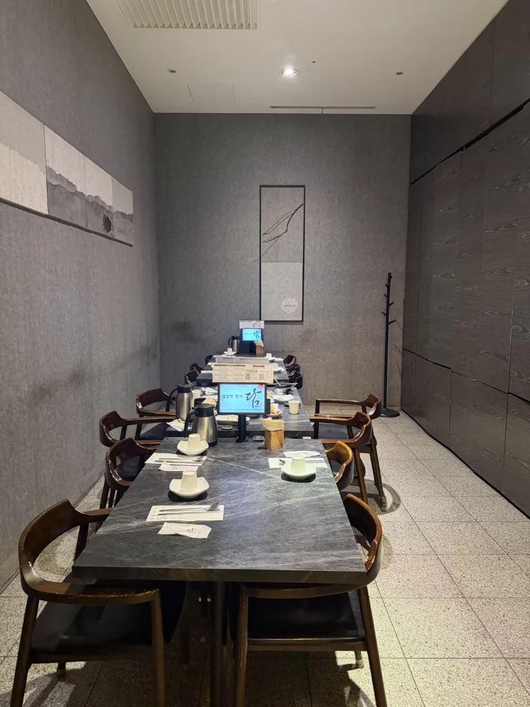 Dam Restaurant private dining room with modern Korean minimalist interior design, stone table, wooden chairs, and calligraphy artwork for traditional hanjeongsik meals at Seoul Arts Center Calligraphy Museum.