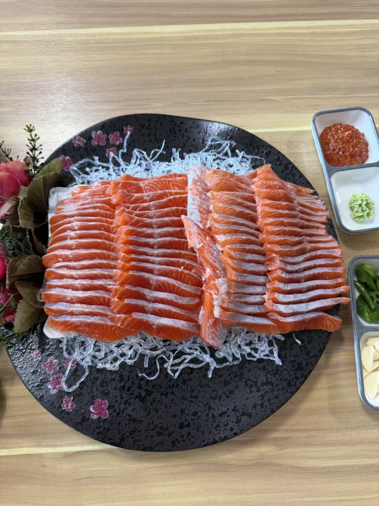 A large platter of freshly sliced Korean trout sashimi (송어회) arranged in rows on shredded radish, served with choganjang, wasabi, sliced green chili, and garlic at Vivaldi Songeogol in Gangwon Province.