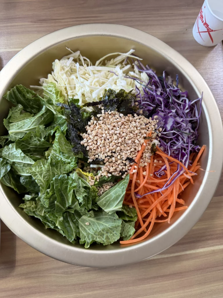 Fresh vegetable salad bowl with shredded cabbage, purple cabbage, julienned carrots, lettuce, dried seaweed, and sesame seeds — the palate-cleansing side dish served alongside Korean trout sashimi (송어회) at Vivaldi Songeogol.