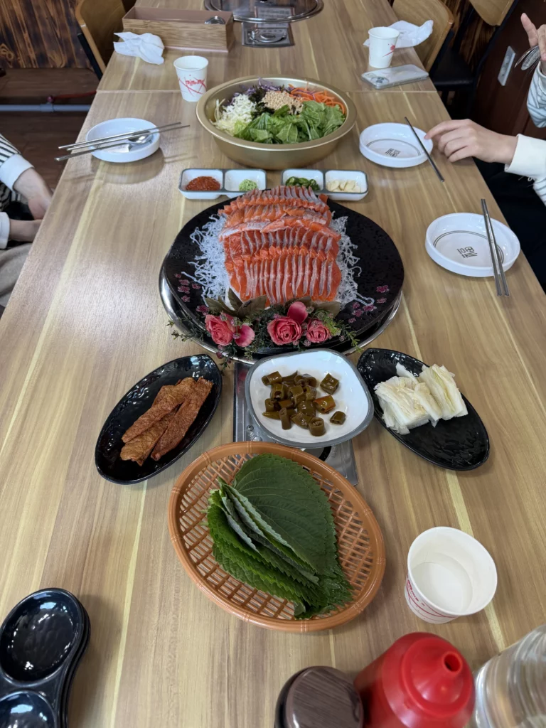 Full Korean trout sashimi (송어회) set at Vivaldi Songeogol, featuring a large platter of freshly sliced trout, perilla ssam leaves, pickled vegetables, dried fish strips, kimchi, dipping sauces, and a vegetable salad bowl — the complete freshwater fish dining spread in Gangwon Province.