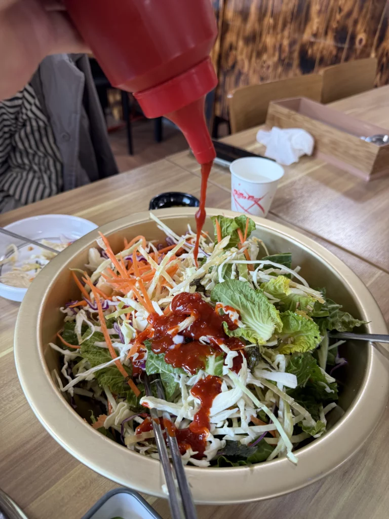 Choganjang (초장) being poured over a fresh vegetable salad bowl to mix and eat alongside Korean trout sashimi (송어회) — a signature palate-cleansing technique unique to freshwater fish dining at Vivaldi Songeogol.