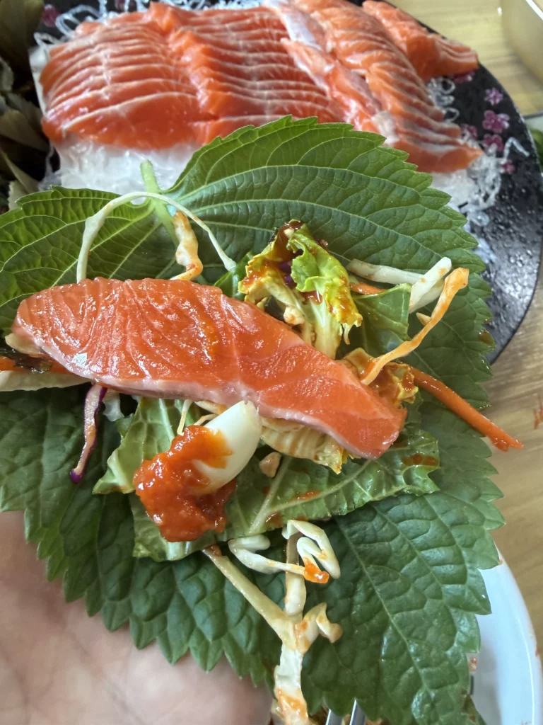 Trout sashimi (송어회) laid over a perilla leaf ssam with mixed fresh vegetables and choganjang — the Korean vegetable-mix eating style that adds crunch and brightness to each bite at Vivaldi Songeogol.