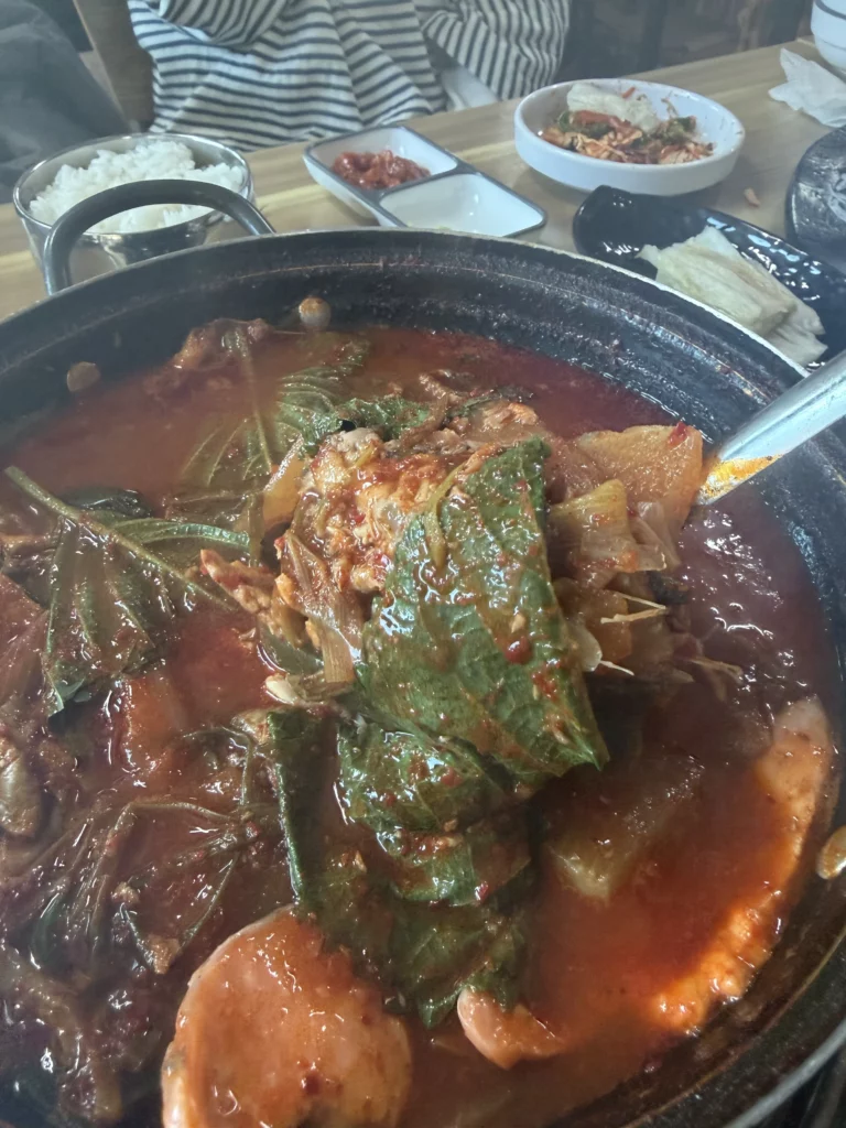 Trout maeuntang (매운탕) simmering in a stone pot with perilla leaves, fish bones, and a deep red gochugaru broth — the traditional spicy stew served as the final course after Korean trout sashimi (송어회) at Vivaldi Songeogol.