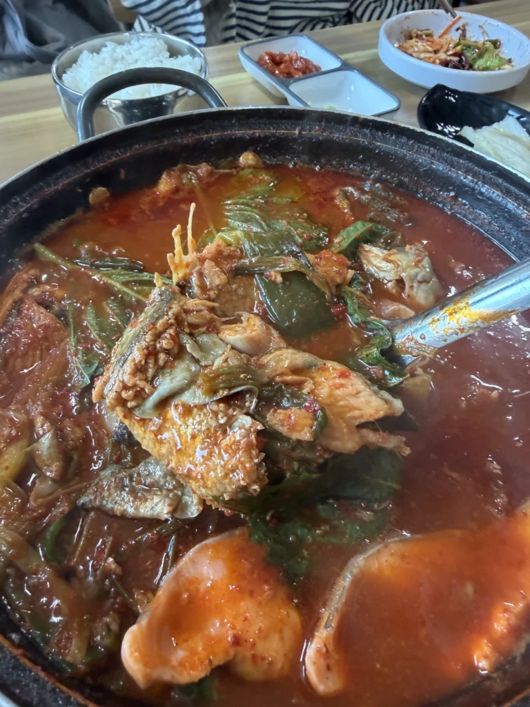 Bubbling spicy trout maeuntang (매운탕) in a stone pot at Vivaldi Songeogol, made from trout bones and head with green onions, vegetables, and gochugaru broth — the traditional finale to a Korean trout sashimi meal.
