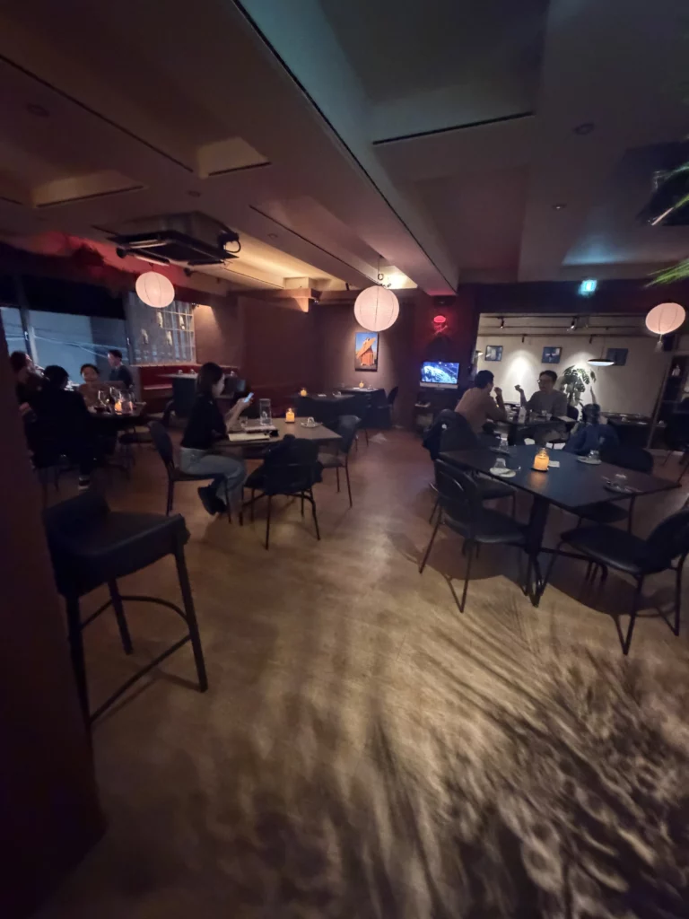 Dimly lit interior of Charari restaurant in Sinsa-dong Seoul, with round paper lanterns hanging from the ceiling, dark tables and chairs occupied by diners, and a warm atmospheric ambiance suited to a modern Korean galbi dining experience.