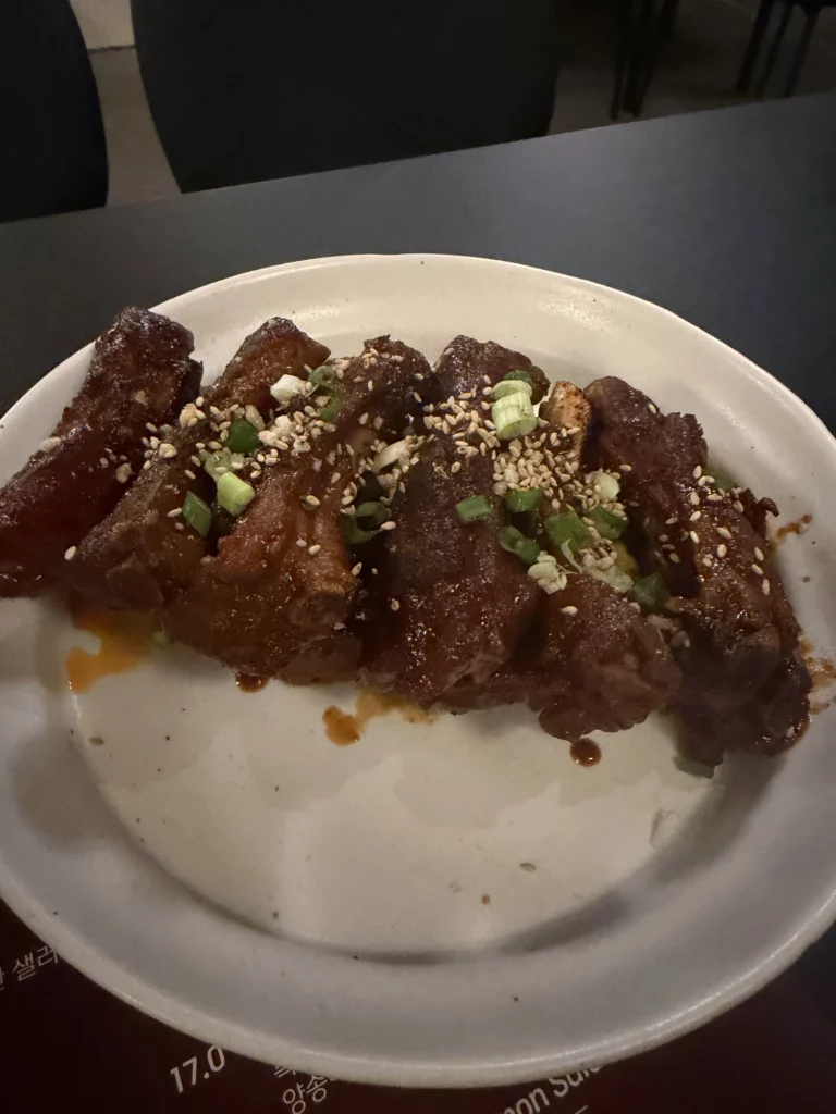 Charari's signature 불등갈비 (fire galbi) served in a white bowl, featuring caramelized back ribs glazed in a rich, dark marinade and topped with sesame seeds and sliced green onions.
