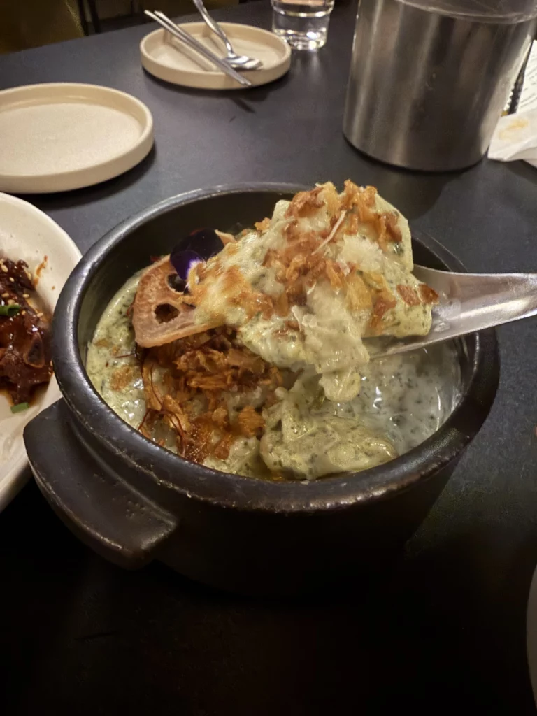 Charari's 미역퓨레 (Miyeok Purée) served in a black stone pot, showing the smooth green seaweed purée topped with a golden crispy layer and dried bonito flakes, with a spoon lifting a portion to reveal its creamy texture.