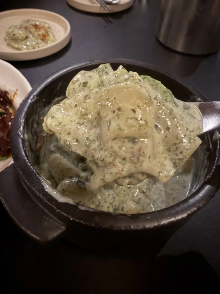 Close-up of Charari's 미역퓨레 (Miyeok Purée) being scooped from a black stone pot, highlighting the thick, silky green seaweed purée texture — a contemporary Korean reinterpretation of traditional miyeok served alongside fire galbi.