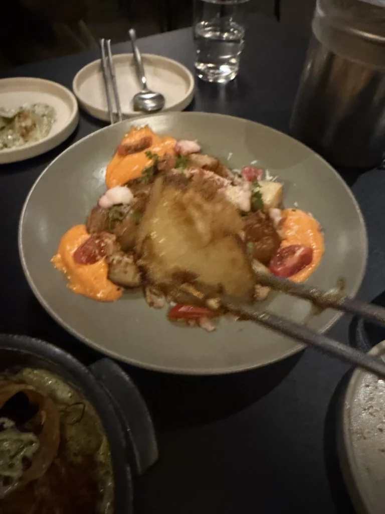 Charari's 오감자 (Ogamja) potato dish served in a grey bowl, featuring a golden-crusted potato topped with vibrant orange sauce, cherry tomatoes, and fresh herb garnish, surrounded by other side dishes on the table.
