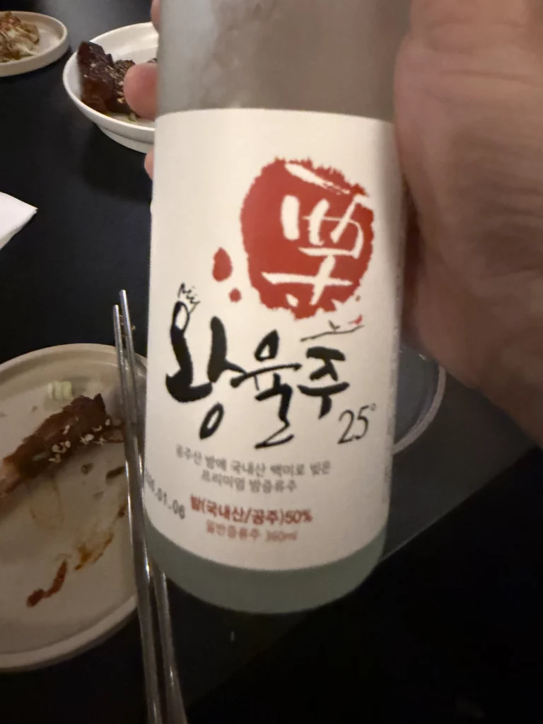 A bottle of 왕율주 25° (Wangyulju), Korea's first chestnut-based distilled spirit, held at the Charari dinner table in Sinsa-dong, with the Korean label and 밤(국내산/공주)50% ingredient detail clearly visible.
