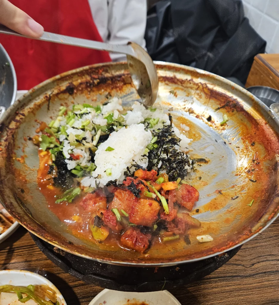 Rice being mixed with seaweed and vegetables in the leftover broth from Won Daegu-tang Cod-fish Hot Pot to make Korean hot pot fried rice.