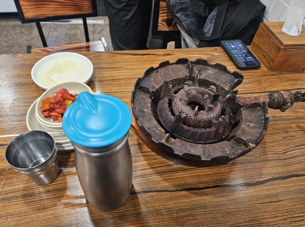 Traditional table setting at Won Daegu-tang restaurant with side dishes and a gas burner prepared for cooking Won Daegu-tang Cod-fish Hot Pot.