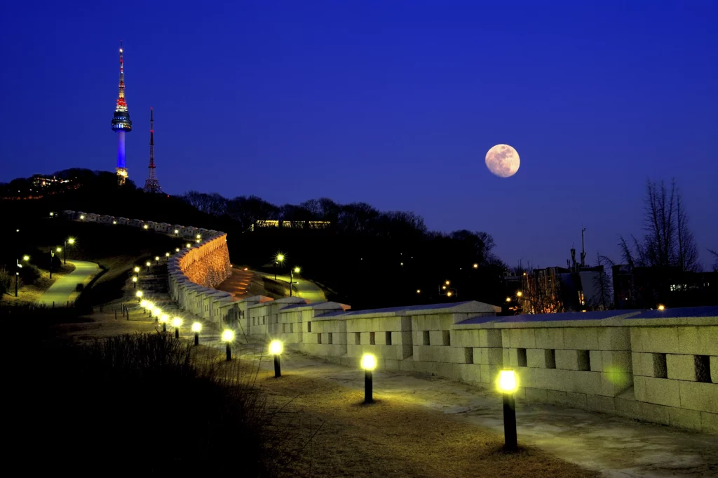 N Seoul Tower illuminated at night on Namsan Mountain with lit pathway along the old city wall, the iconic landmark where Durumi Bunsik is located.