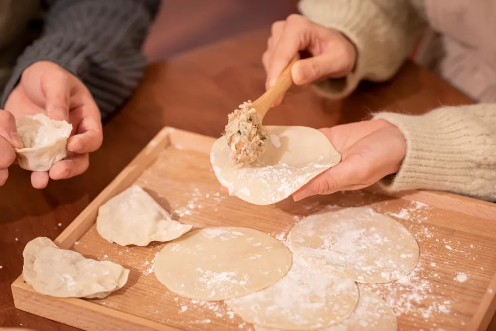 Hands filling fresh mandu wrappers with pork and vegetable mixture in the traditional Bukchon Son Mandu handmade dumpling style.