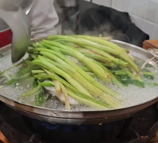 Won Daegu-tang Cod-fish Hot Pot boiling with fresh water parsley and cod fish in a bubbling Korean seafood hot pot at Won Daegu-tang restaurant.