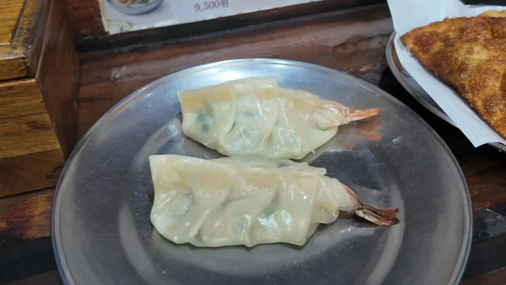 Bukchon Son Mandu shrimp mandu with whole shrimp tails served steamed on a metal plate.