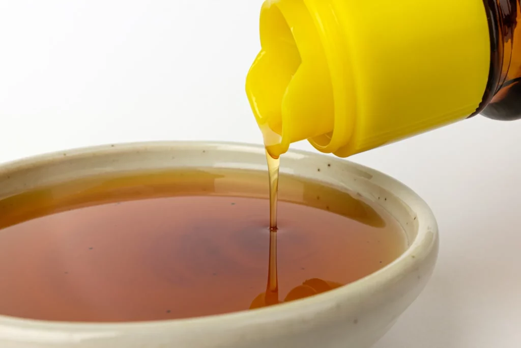 Korean toasted sesame oil being poured from a yellow-capped bottle into a ceramic bowl — a key finishing ingredient in Korean bibimbap