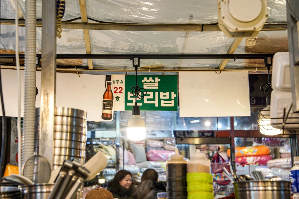 Green overhead sign reading 쌀 보리밥 (Rice Barley Bowl) with Dongbu A-22 stall number, hanging inside Gwangjang Market — the landmark sign for Gabose Bibimbap