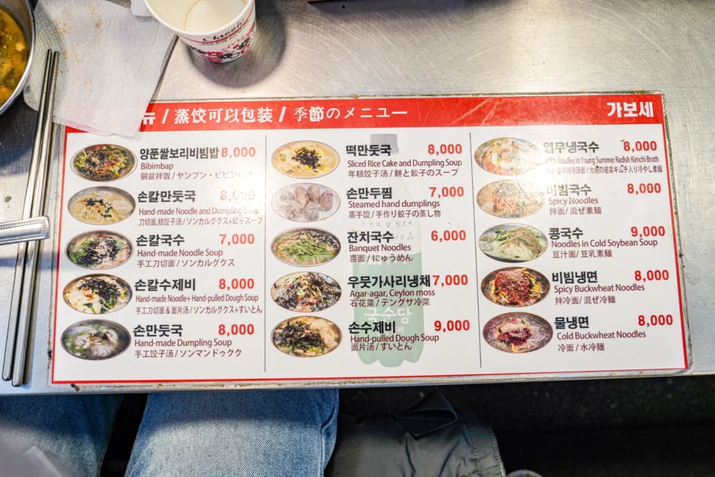 The full laminated menu board of Gabose Bibimbap at Gwangjang Market Stall A22, showing dish names and prices in Korean, Chinese, and Japanese, ranging from 6,000 to 9,000 won
