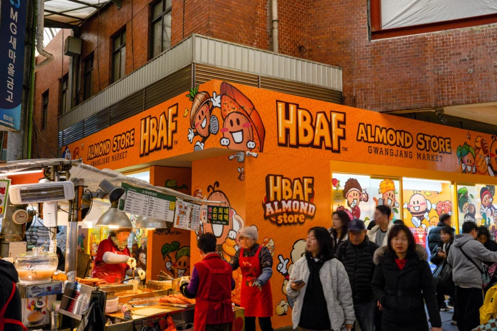 HBAF almond store interior at Gwangjang Market with product displays and the market's bustling food corridor in the background.
