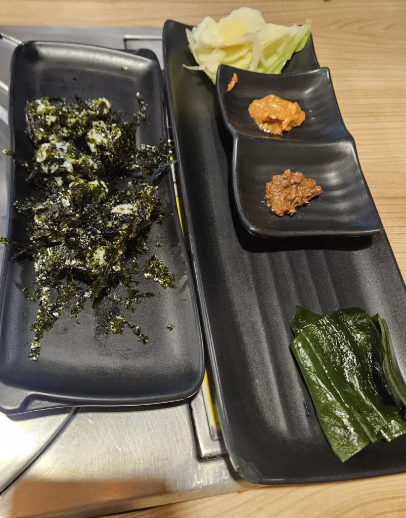 Agujjim: Garosu-gil Braised Monkfish meal served with Korean side dishes including seaweed rice balls, kelp, garlic, and ssamjang dipping sauces on a restaurant table in Garosu-gil.