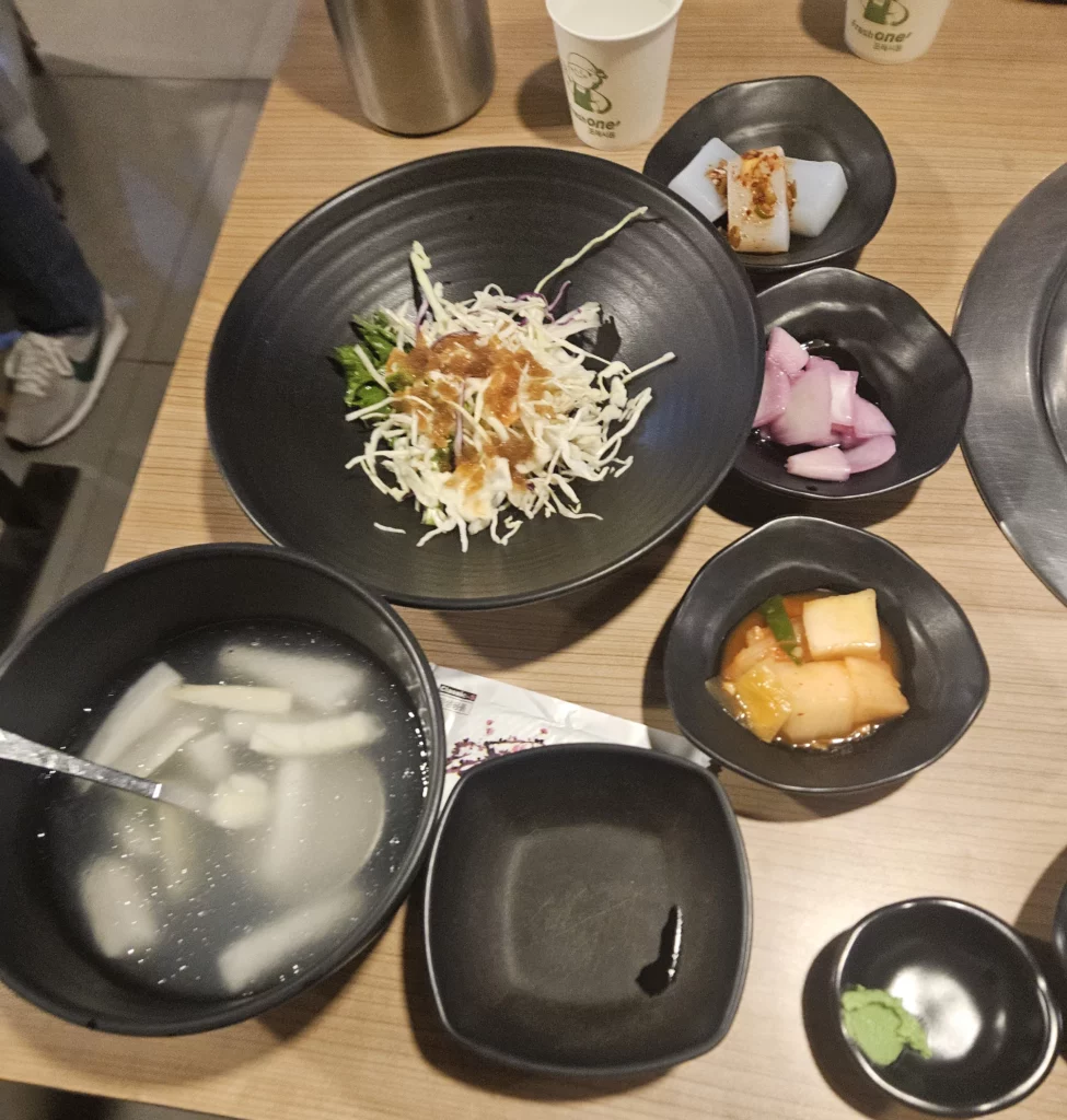 Agujjim: Garosu-gil Braised Monkfish meal served with Korean side dishes including cabbage salad, pickled radish kimchi, pickled onions, and a bowl of dongchimi radish soup on a restaurant table in Garosu-gil.
