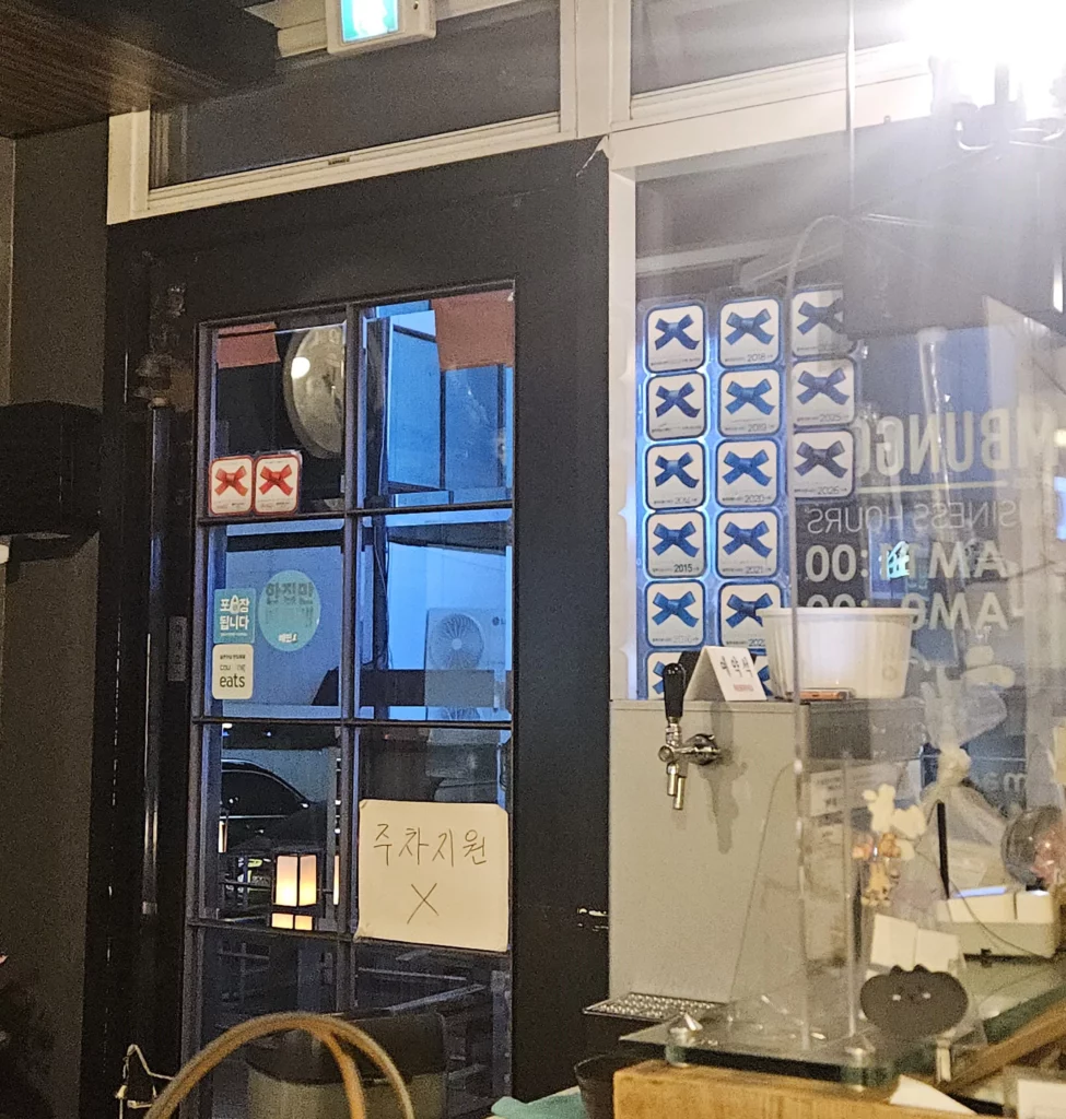 Agujjim: Garosu-gil Braised Monkfish restaurant interior entrance at Chimbungga in Garosu-gil, showing the door, award stickers, and dining area atmosphere inside a Korean traditional seafood restaurant.