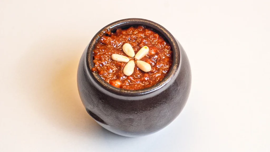 Traditional Korean gochujang fermented chilli paste in a dark ceramic jar, garnished with pine nuts — the essential sauce for authentic bibimbap