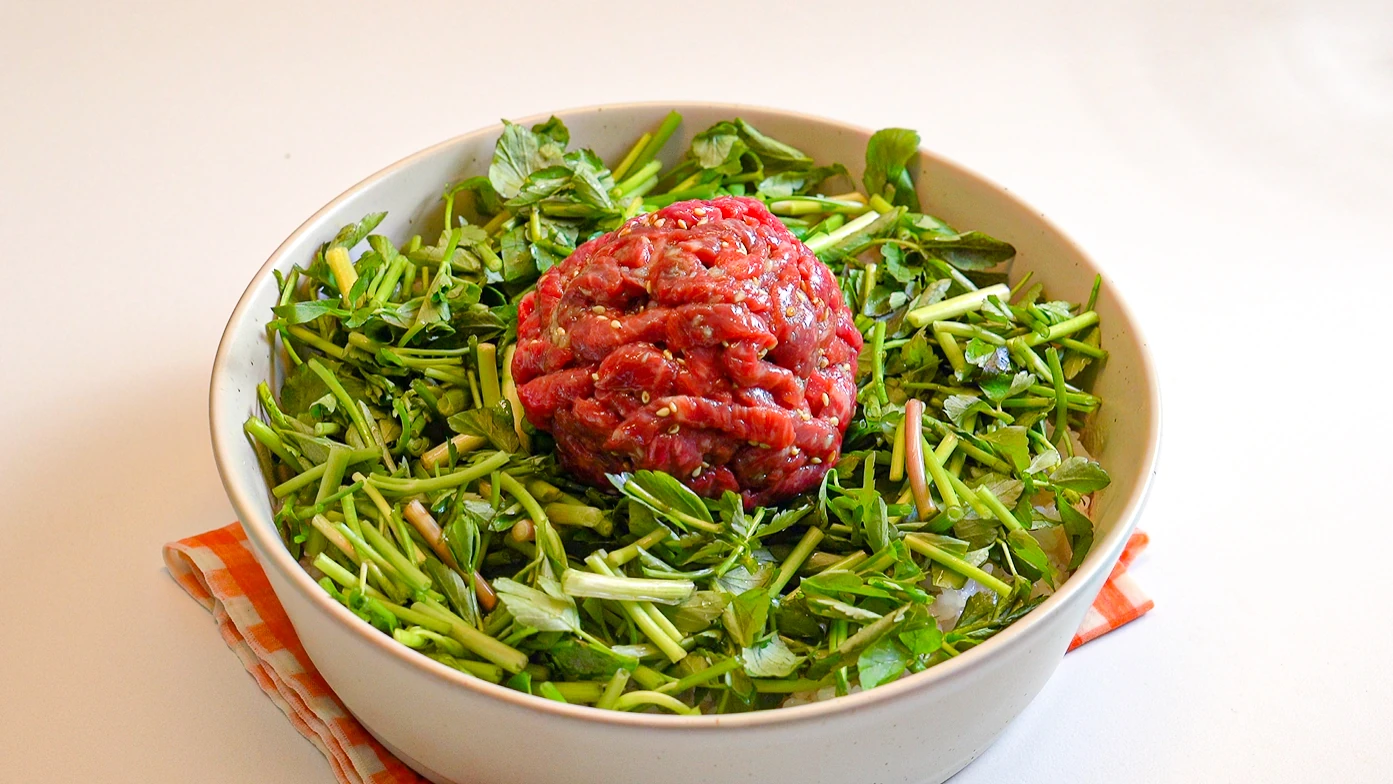 Finished yukhoe bibimbap bowl with seasoned raw beef strips layered over white rice and fresh minari, ready to serve.