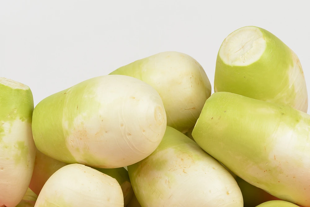 Several whole Korean radishes with greenish tops piled together — the defining ingredient slow-cooked as shredded radish to create Gangga-ne Tteokbokki's signature radish broth